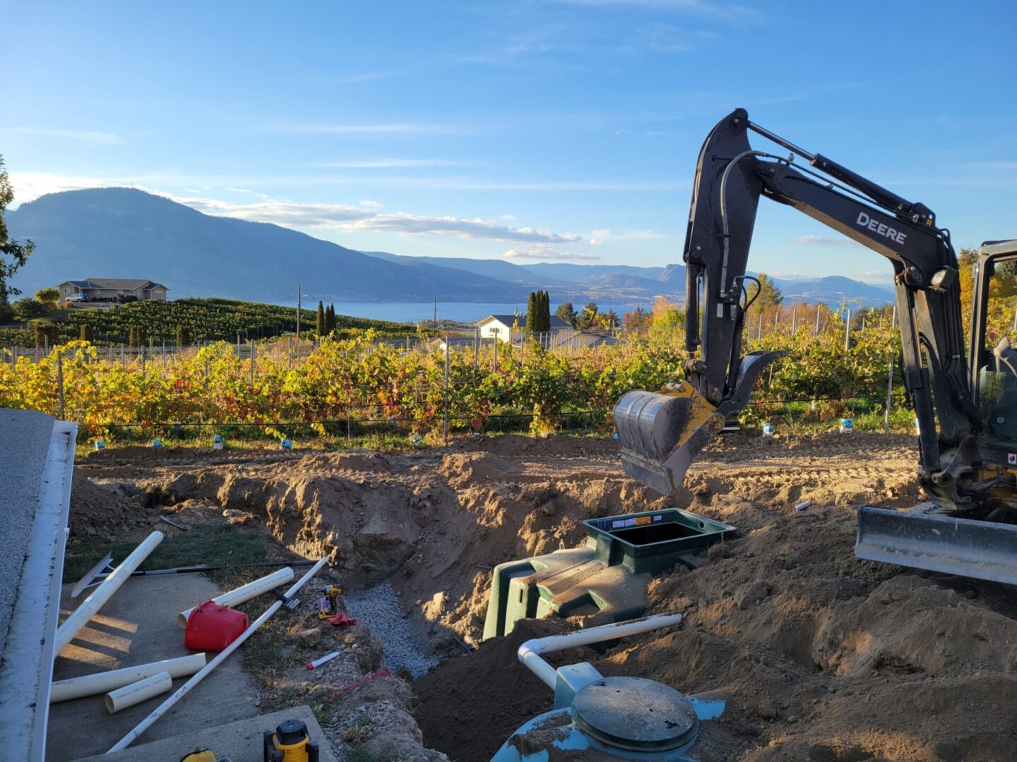 A backhoe is digging in the dirt near some pipes.