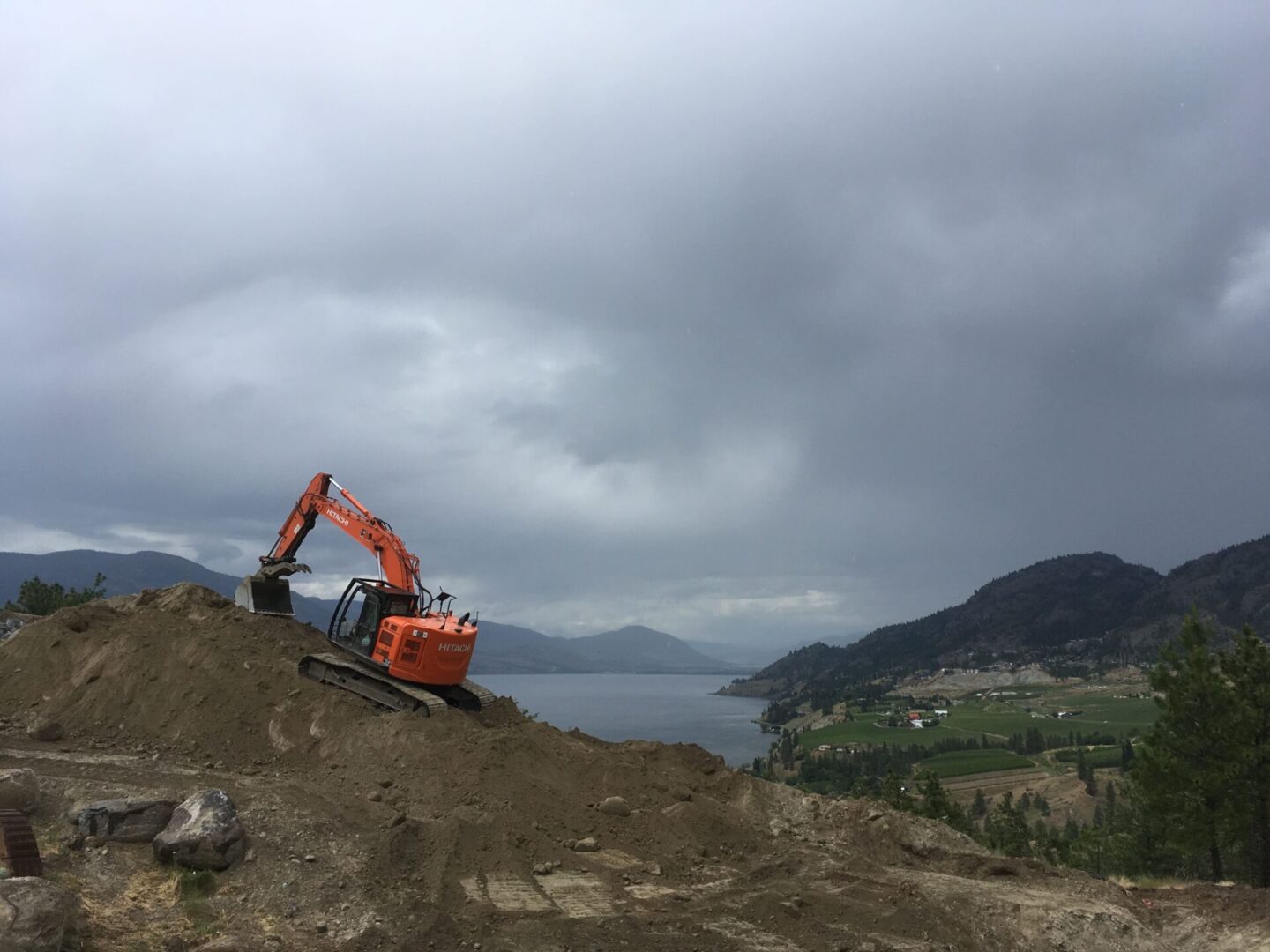 A large orange and black excavator on top of a hill.